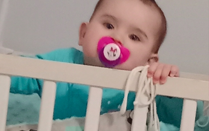 Małe dziecko z smoczkiem, trzymające się barierki łóżeczka.