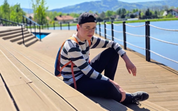 Młody chłopak siedzący na drewnianym tarasie nad wodą.