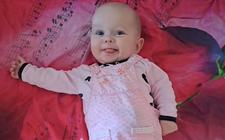 Uśmiechnięta niemowlę w różowym ubranku, leżące na kolorowej pościeli.