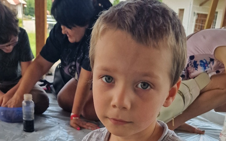 Chłopiec z poważnym wyrazem twarzy, w tle inni ludzie.