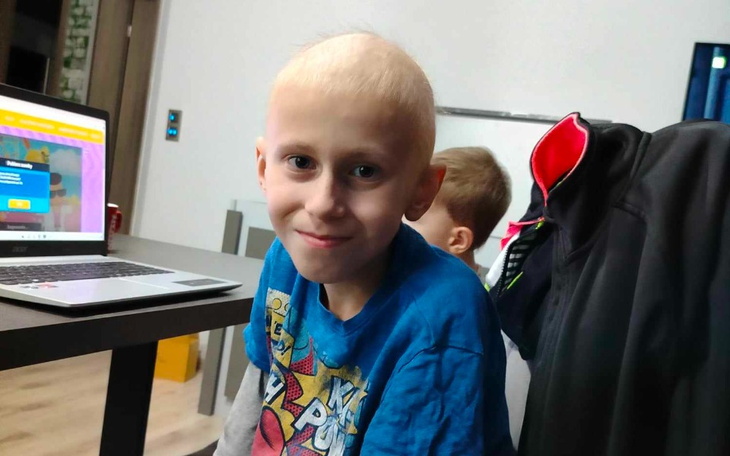 Chłopiec z uśmiechem siedzący przy biurku z laptopem.