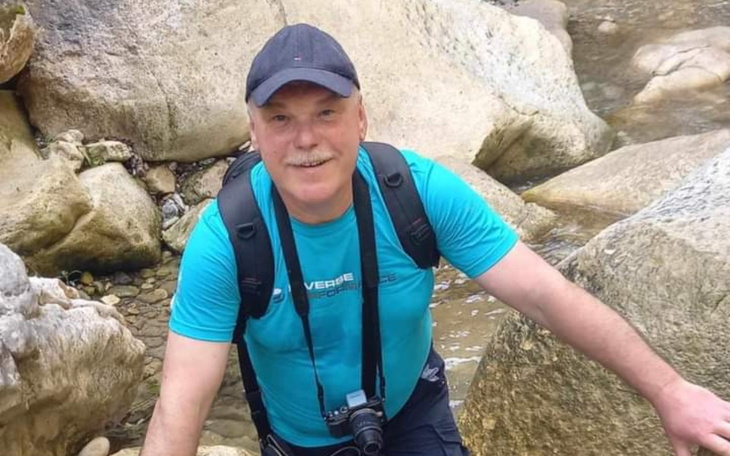 Mężczyzna w niebieskiej koszulce na tle skał i wody.