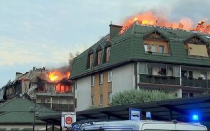 Pożar na dachu budynku, ogień i dym widoczne z daleka.