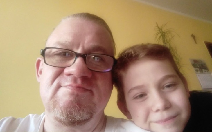 Mężczyzna z chłopcem, uśmiechnięci w domowym otoczeniu.