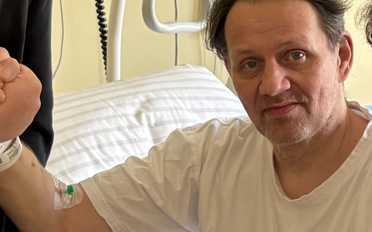 Mężczyzna na oddziale szpitalnym uśmiecha się do kamery, z opaską na nadgarstku.
