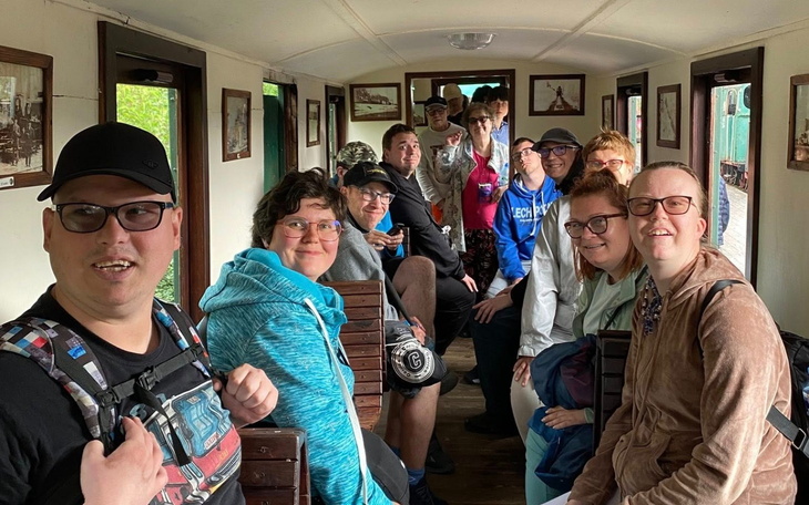 Grupa ludzi w wagonie, uśmiechnięci i zadowoleni.