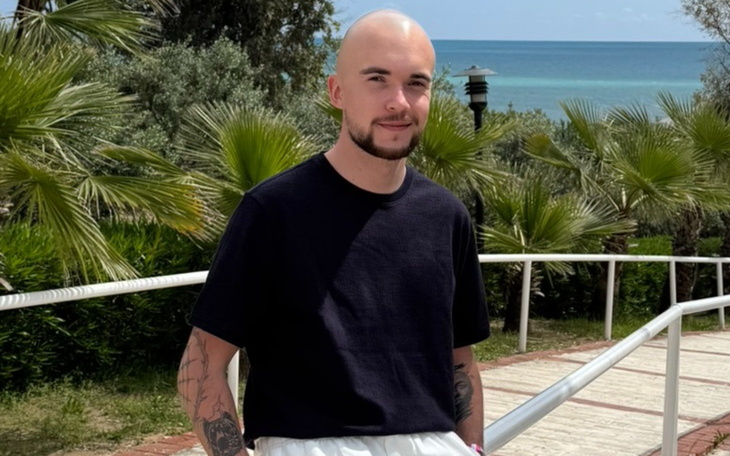 Młody mężczyzna na tle morza, uśmiechający się do kamery.