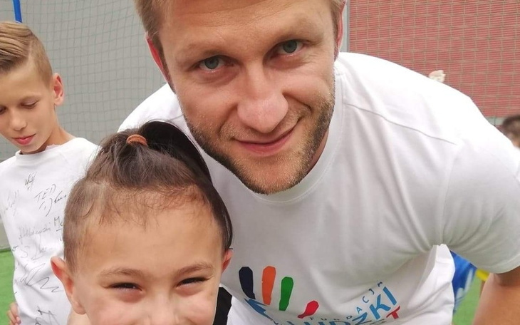 Uśmiechnięta dziewczynka z dorosłym na boisku sportowym.