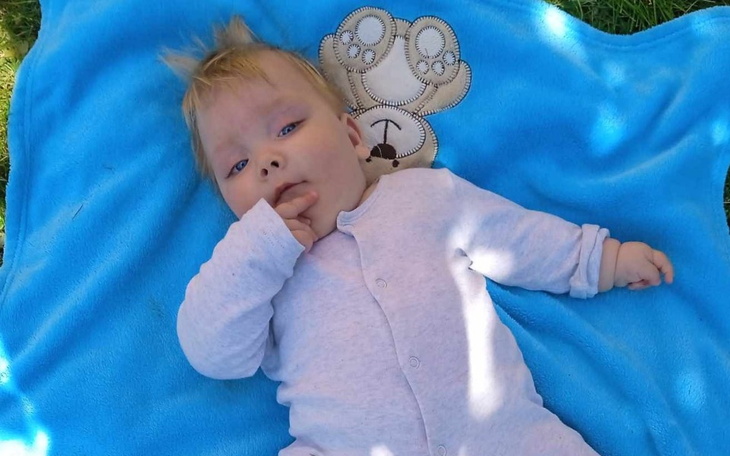 Małe dziecko leżące na niebieskim kocyku, ssące kciuk.