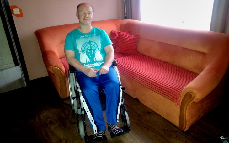 Mężczyzna na wózku inwalidzkim, siedzący na kanapie.