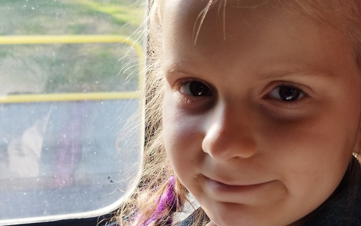 Uśmiechnięta dziewczynka w autobusie, z blaskiem w oczach.