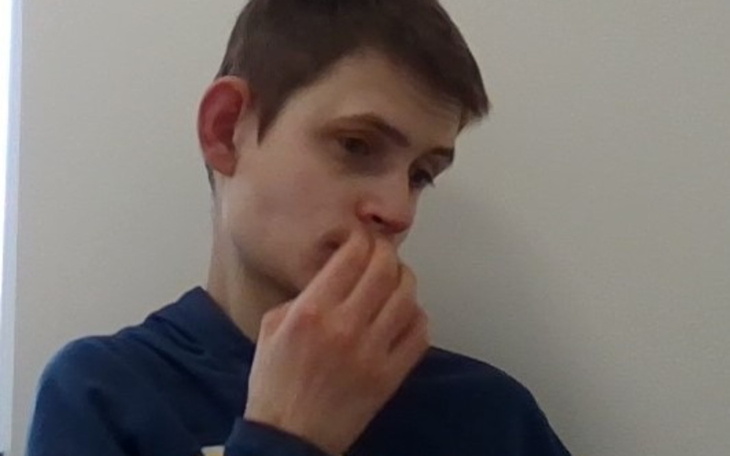 Młody mężczyzna zamyślony, siedzący w pomieszczeniu.