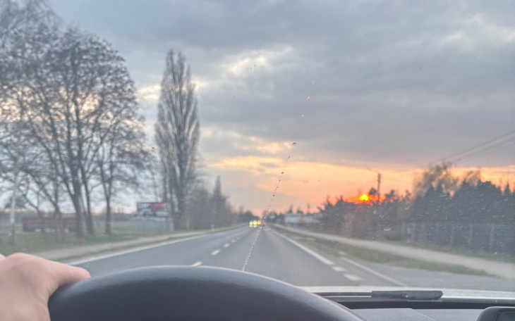 Widok na drogę podczas zachodu słońca, z ręką na kierownicy.