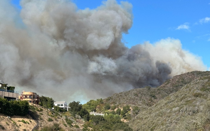 Widok na dym unoszący się nad wzgórzami, w tle domy.