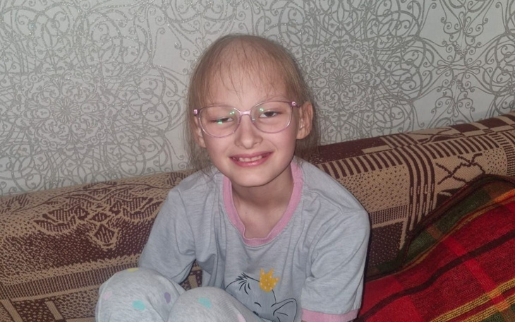 Uśmiechnięta dziewczynka w okularach na kanapie.