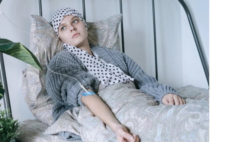 Młoda kobieta w szpitalnym łóżku, z opaską na głowie i kroplówką.