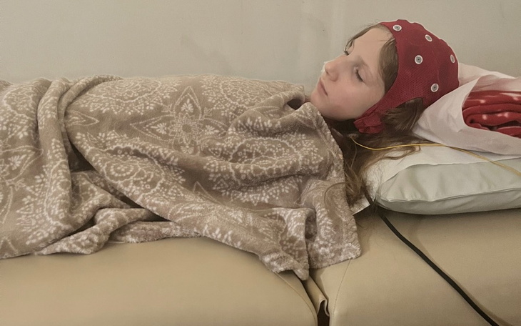 Dziewczynka leżąca na łóżku z opaską na głowie, w otoczeniu kabli.