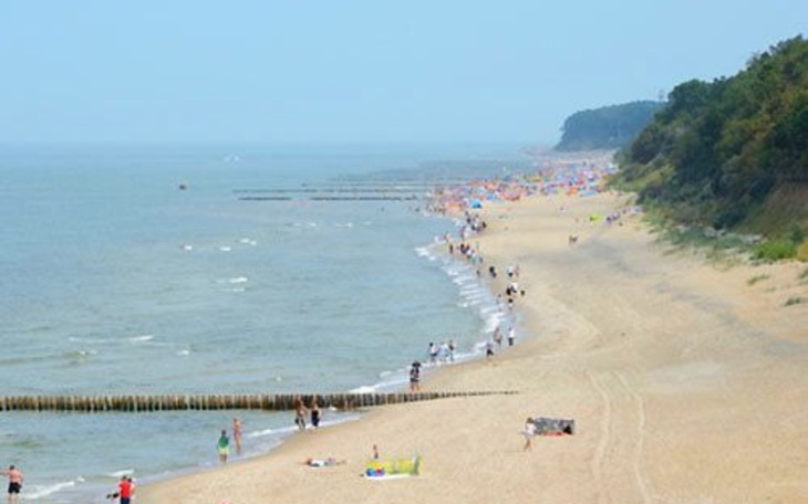 Plaża z ludźmi, parasolami i falami morskimi w tle.