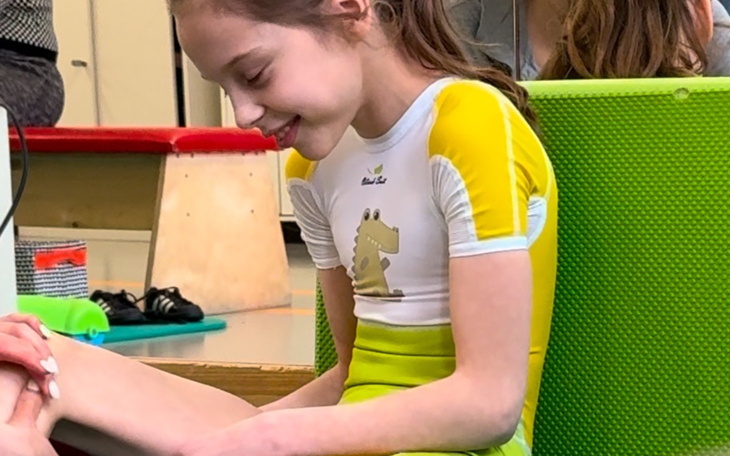 Dziewczynka w stroju gimnastycznym, uśmiechająca się.