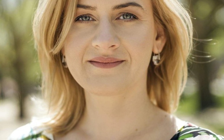 Portret kobiety w jasnej bluzce, uśmiechającej się na tle zieleni.