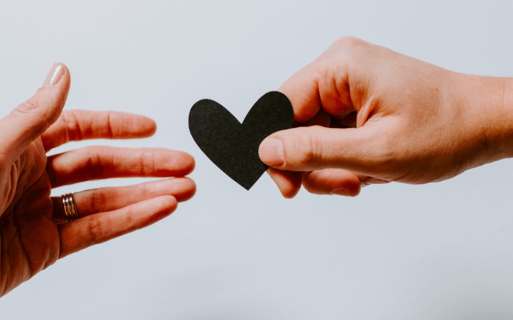 Dwie ręce sięgające po czarny papierowy serce, symbolizujące miłość.