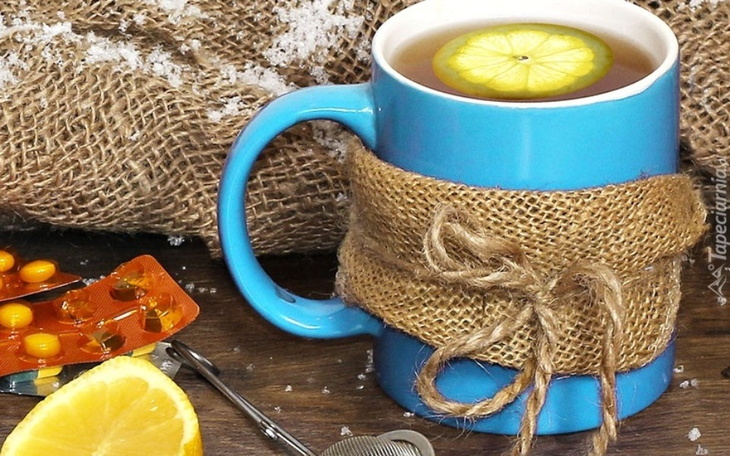 Herbata z cytryną w niebieskiej filiżance, otoczona cytryną i lekami.