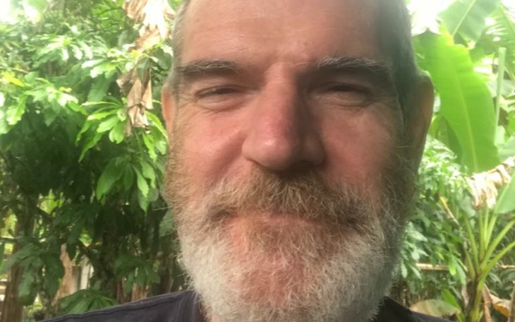 Mężczyzna z brodą uśmiechający się w otoczeniu zieleni.