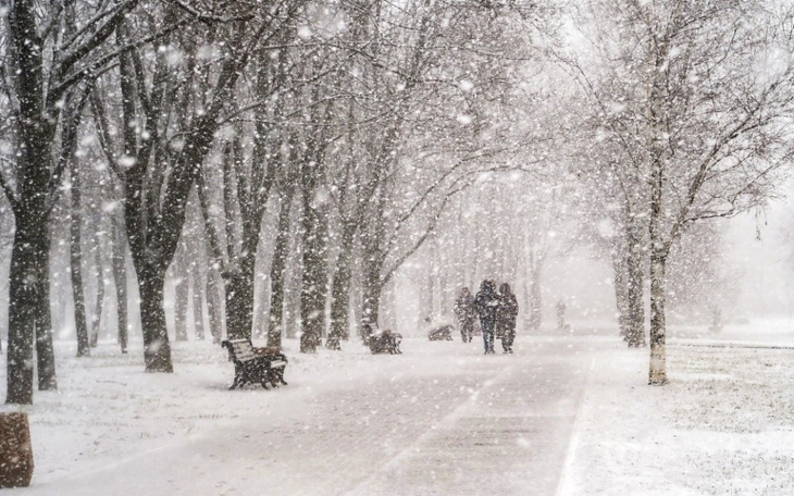 Zimowy krajobraz z padającym śniegiem i spacerującymi ludźmi.