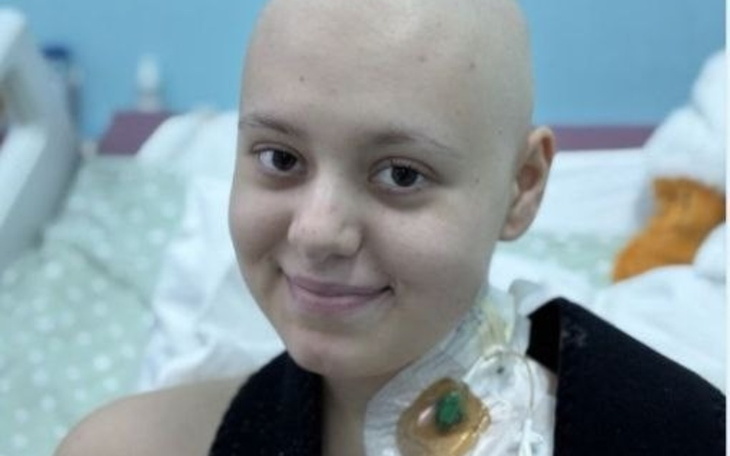 Młoda dziewczyna z uśmiechem, w szpitalnym łóżku, z opatrunkiem na szyi.