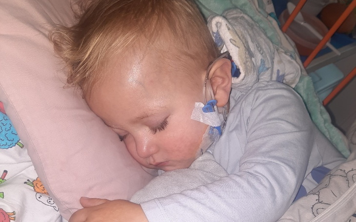 Chłopczyk śpiący w szpitalnym łóżku, z opatrunkiem na głowie.