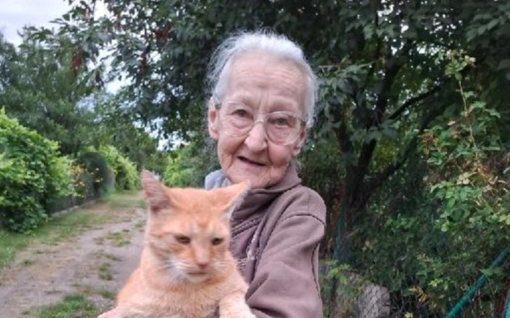 Starsza kobieta trzymająca kota na tle zieleni.