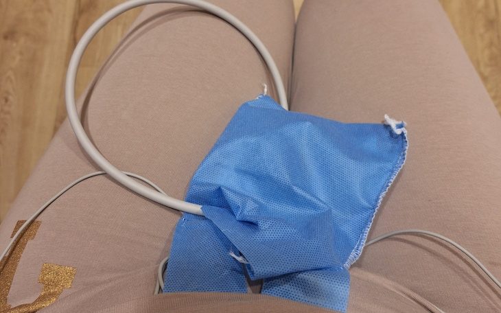 Osoba siedząca z niebieską maską i przewodami medycznymi.