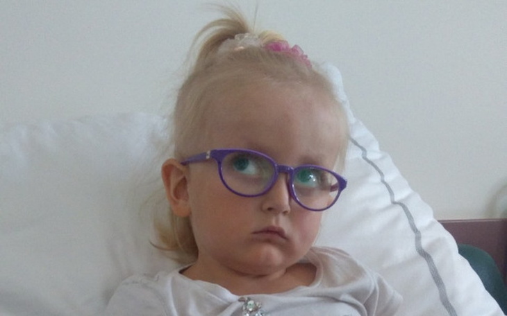Mała dziewczynka w szpitalu, nosząca okulary, z poważnym wyrazem twarzy.