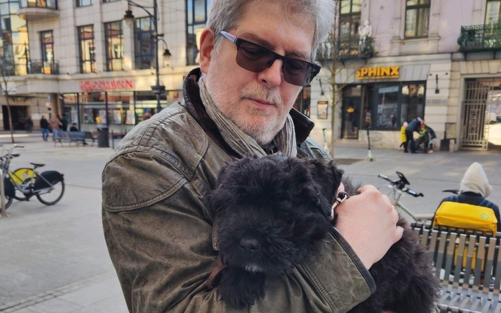 Mężczyzna z okularami trzymający szczeniaka w ramionach.