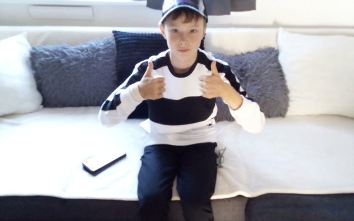 Chłopiec z kciukami w górze, siedzący na kanapie.