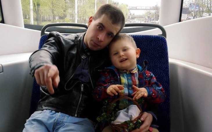 Mężczyzna z dzieckiem na rękach, obaj uśmiechnięci w autobusie.