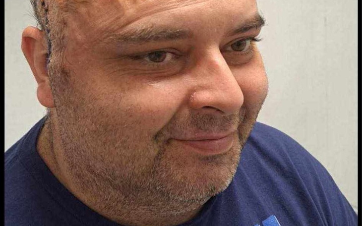 Mężczyzna w okularach, zadowolony na tle szarej ściany.