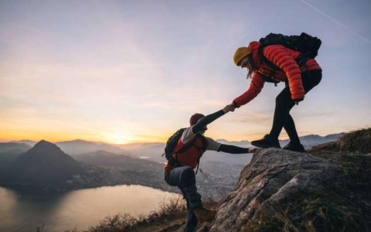 Dwoje wspinaczy na szczycie góry, pomagających sobie nawzajem.