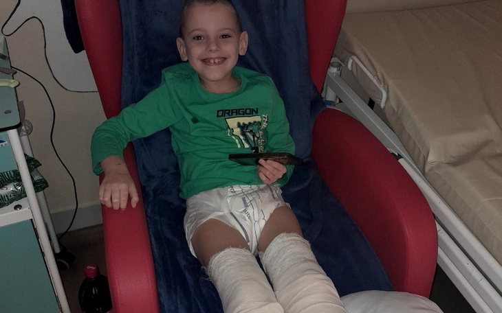 Chłopiec w szpitalu uśmiecha się, siedząc na czerwonym fotelu.