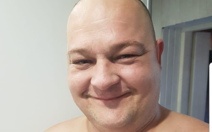 Mężczyzna z uśmiechem, w bluzie, w domowym otoczeniu.