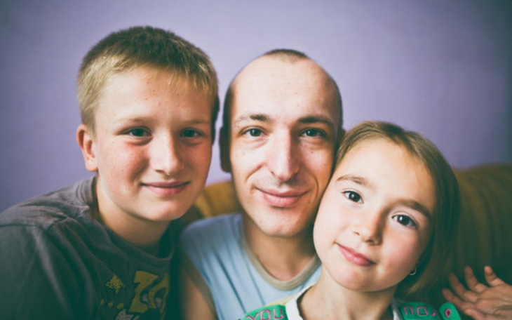 Uśmiechnięty mężczyzna z dwójką dzieci na tle fioletowej ściany.