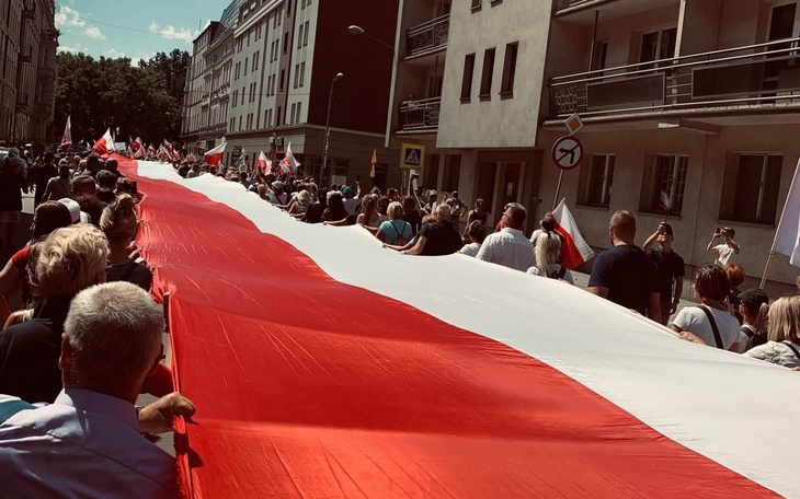Manifestacja z flagą Polski, tłum ludzi na ulicy.