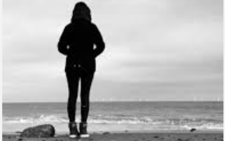 Osoba stojąca na plaży, patrząca na morze w czerni i bieli.