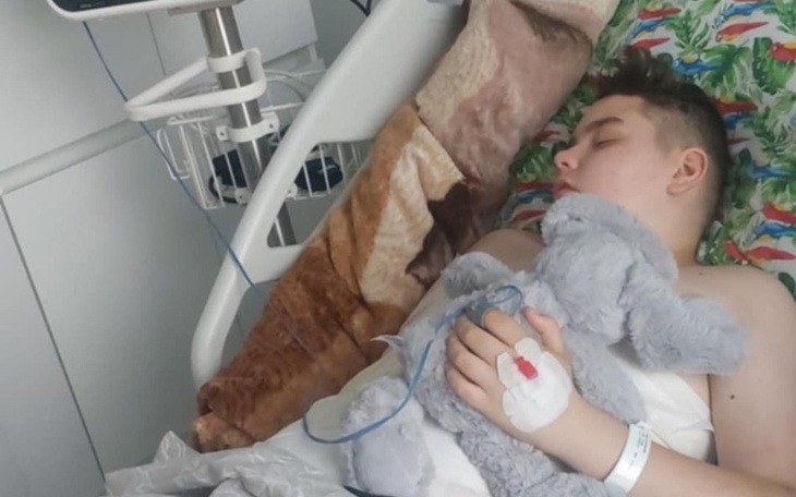 Chłopiec leżący w szpitalu, trzymający pluszowego misia.