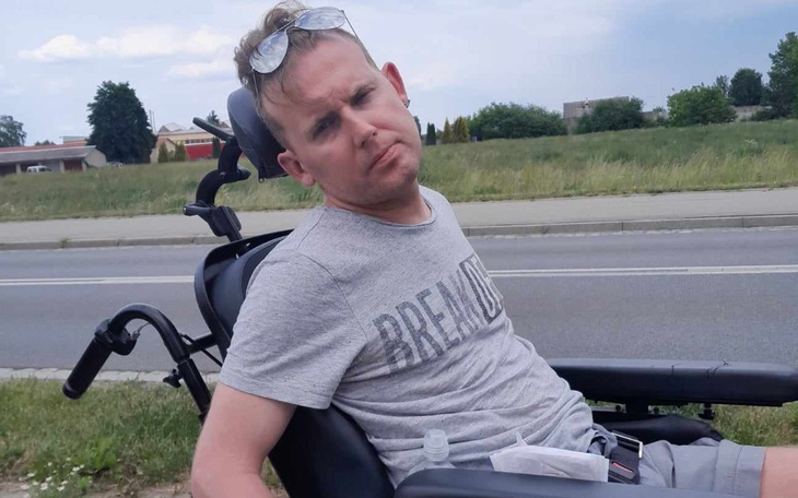 Mężczyzna na wózku inwalidzkim, siedzący na trawie przy drodze.