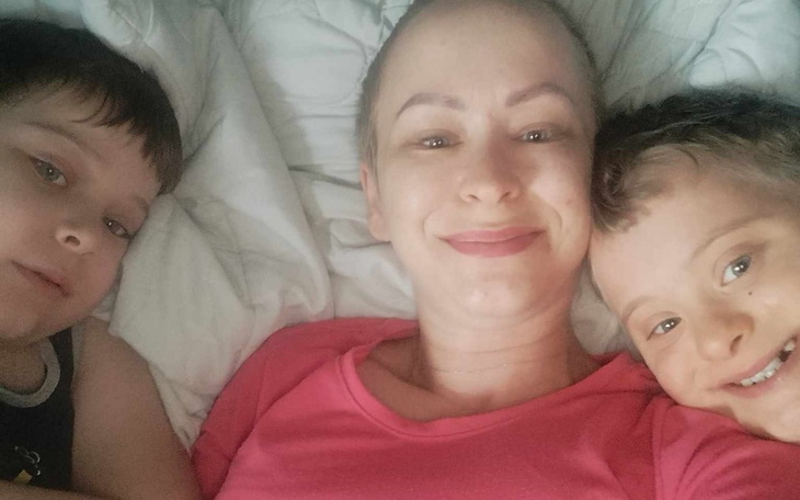 Kobieta z dwoma dziećmi, wszyscy uśmiechnięci w łóżku.