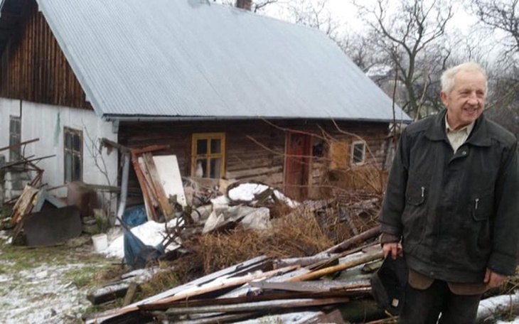 Mężczyzna przy starym domu, otoczony przez bałagan.