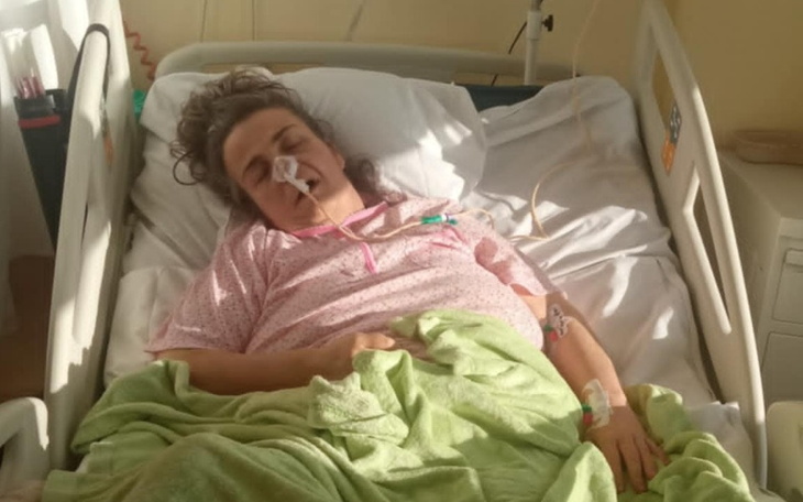 Kobieta w szpitalnym łóżku, z widocznymi rurkami i kocem.