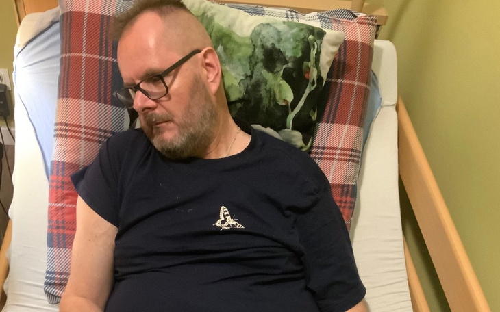 Mężczyzna leżący na łóżku, z zamkniętymi oczami, w okularach.