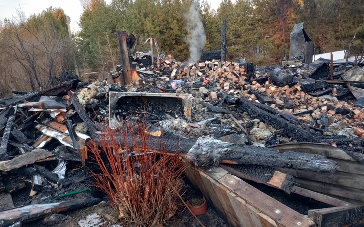 Zniszczony dom po pożarze, z ruinami i dymem w tle.